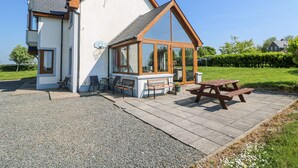 A two-story house with a patio area featuring a wooden table and chairs, a basketball hoop, and a large glass window. - Lacey's Harbour (Battlestown)