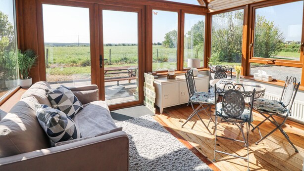 A spacious room with a wooden ceiling, large windows, a sofa, a dining table with chairs, and a small kitchen area. - Lacey's Harbour (Battlestown)