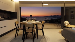 Un comedor moderno con una mesa dispuesta para cuatro personas, un sofá y vistas a un atardecer sobre un paisaje urbano.