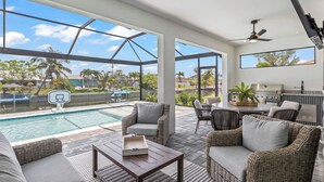 Ein moderner Außenbereich mit Pool, Korbmöbeln und einem großen Fenster mit Blick auf Palmen und einen klaren Himmel.