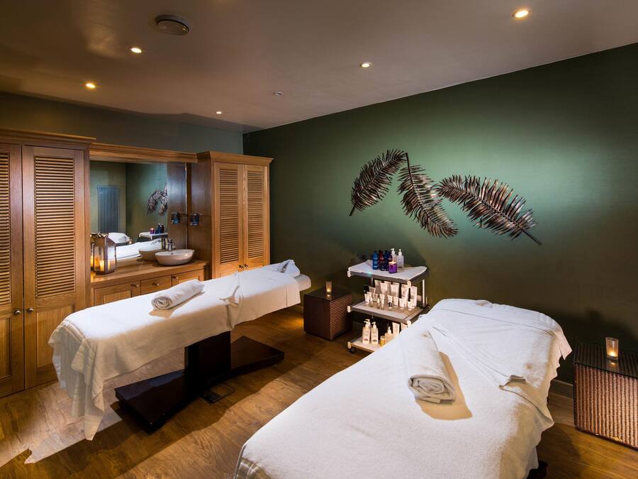 Un cuarto de spa con dos camas, un espejo grande, armarios de madera y una planta suspendida en la pared.