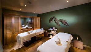 Ein Wellnessraum mit zwei Betten, einem großen Spiegel, Holzschränken und einer Wandpflanze.