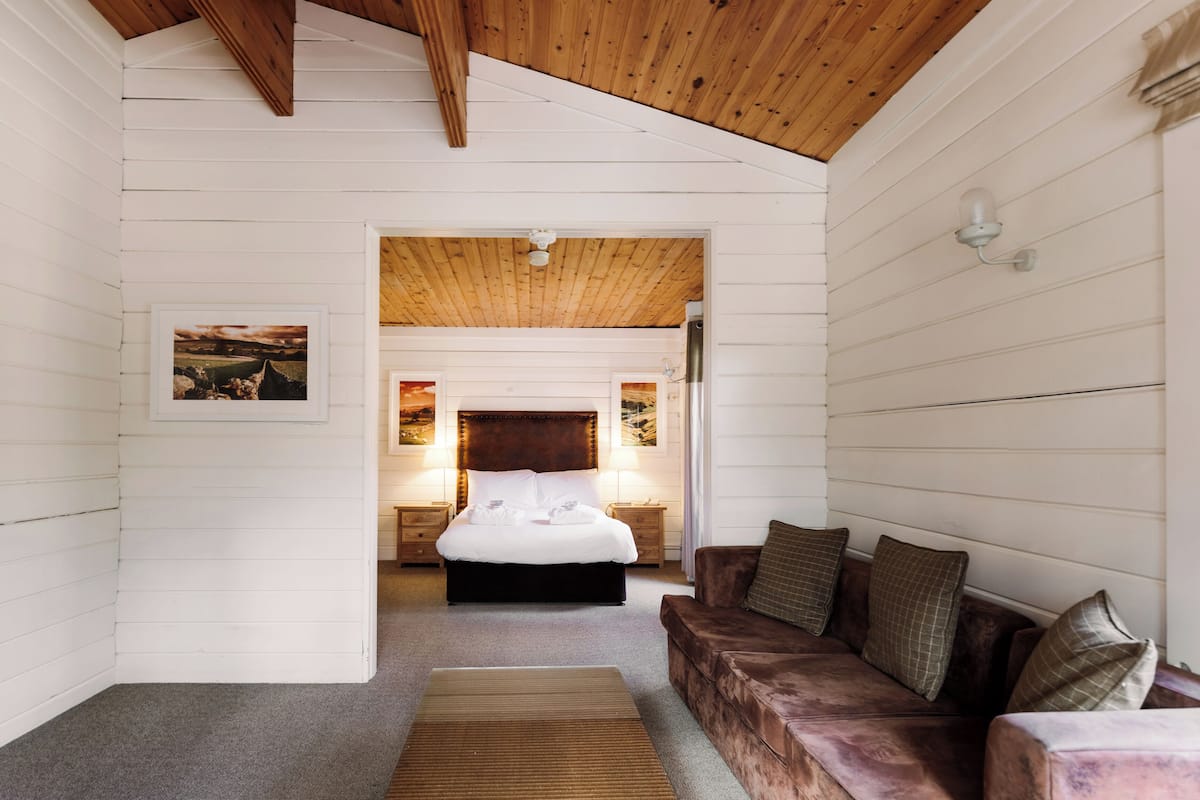 Ein Schlafzimmer mit Holzbalkendecke, einem Bett mit weißen Leinen, einem braunen Ledersofa und einem kleinen Teppich.