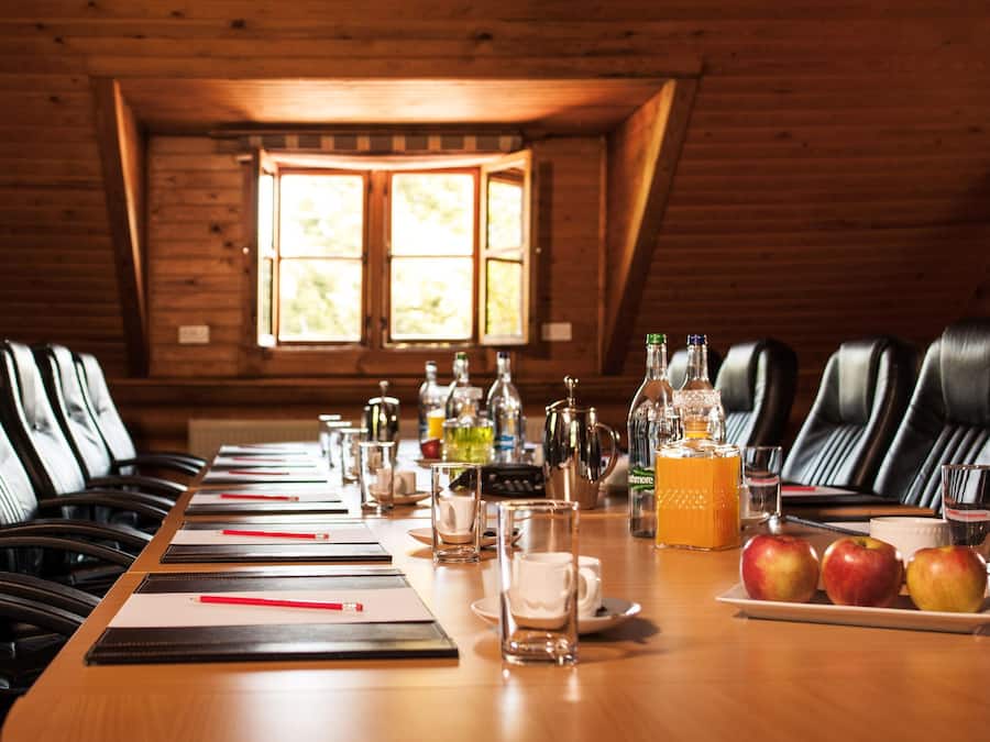 A conference room with leather chairs, a long table, and various items like bottles, glasses, and apples.