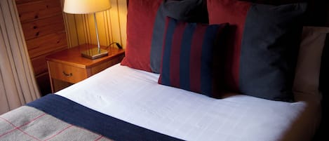 A neatly made bed with a plaid blanket, a bedside lamp, and striped pillows.