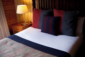 Ein ordentlich bezogenes Bett mit einer karierten Decke, einer Nachttischlampe und gestreiften Kissen.