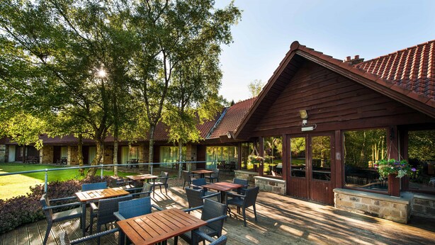 Une terrasse extérieure avec des tables et des chaises en bois, un espace salon abrité et une vue sur un terrain de golf.