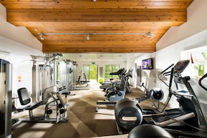Un gimnasio con diverso equipo de ejercicios, techo de madera y ventanas amplias.