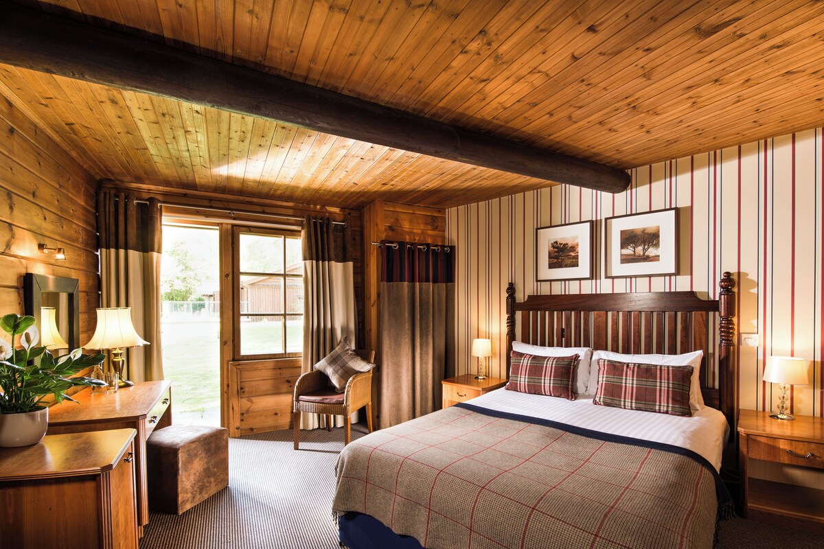 Een slaapkamer in blokhutstijl met een groot bed, twee nachtkastjes, een stoel en een raam.