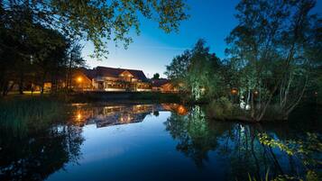 A lakeside hotel with a reflection in the water, surrounded by trees and a well-lit building.