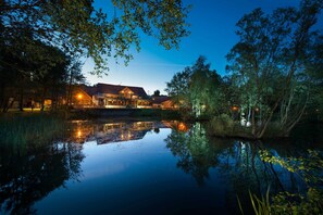 Un hôtel situé au bord d’un lac, dont le reflet se mire dans l’eau, entouré d’arbres et dont le bâtiment est bien éclairé.