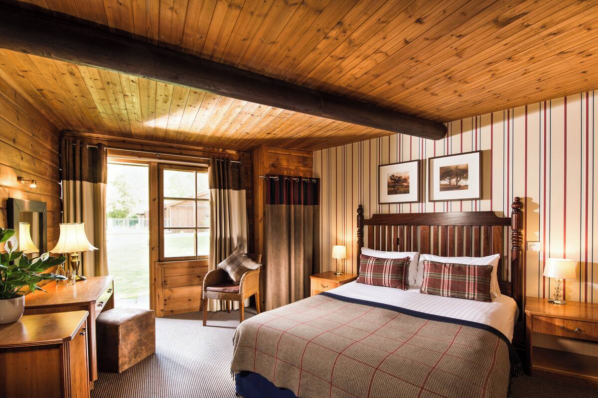 Ein schlafzimmerähnlicher Holzblock mit einem großen Bett, zwei Nachttischen, einem Sessel und einem Fenster.