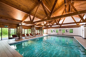 Une piscine intérieure avec des poutres en bois, des chaises longues et un mur en pierre.