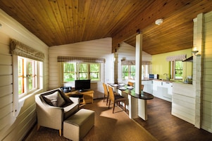 Interior acolhedor de cabana com teto de madeira, área de jantar com mesa e cadeiras, sofá e televisão.