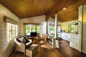 A cozy cabin interior with a wooden ceiling, a dining area with a table and chairs, a sofa, and a television. - Chevin Country Park Hotel (Otley)