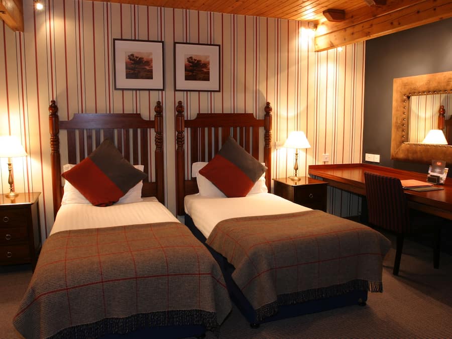 Quarto de hotel com duas camas, uma escrivaninha, uma cadeira e um espelho.