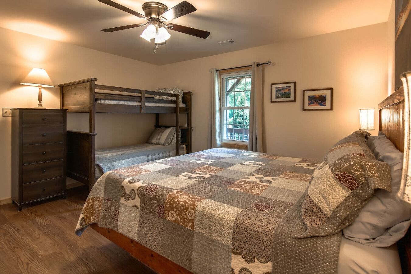 Un dormitorio con una cama litera, un aparador, un ventilador de techo y una ventana con cortinas.