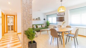 A modern living room with a stone accent wall, a dining area with a round table and chairs, a green sofa, and a large window with a view. - Your Ideal Base to explore Zaragoza`s delights (Zaragoza)