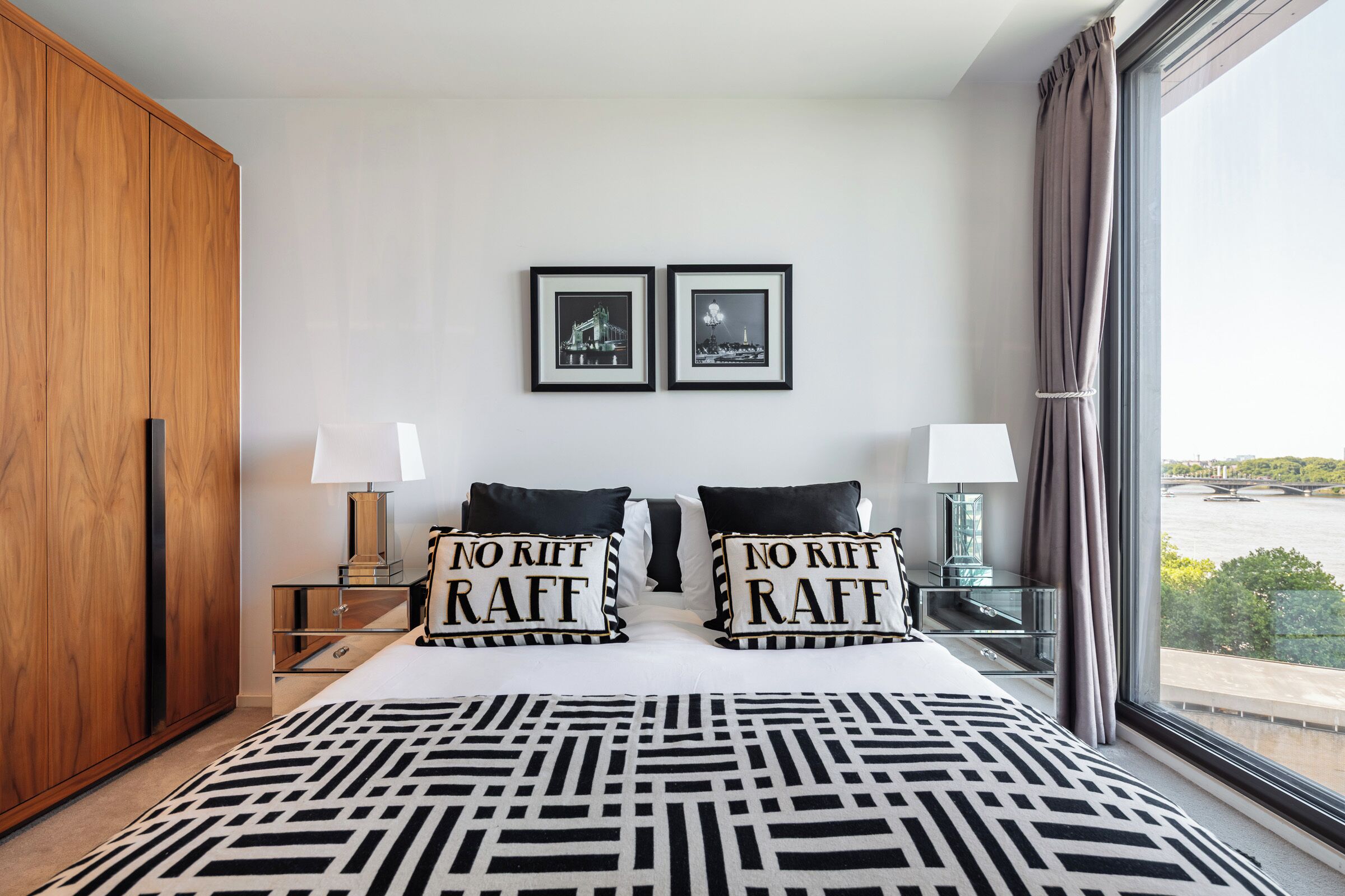 A hotel room with a large bed, two bedside tables with lamps, a wardrobe, and two framed pictures on the wall.