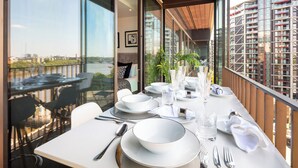 Comedor con mesa lista para cuatro personas, ventanas amplias y vista panorámica de la ciudad.