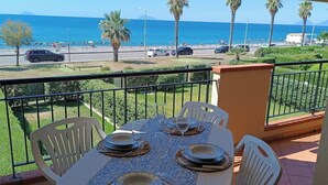 A balcony with a table set for dining, overlooking a coastal road with palm trees and a clear view of the sea. - VACATION HOME SUN & BEACH - LEMONS APARTMENT (Capo d'Orlando)