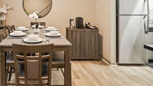 A dining area with a wooden table set for four, a round mirror above, and a kitchen with a white refrigerator and wooden cabinets. - King Bed, 5 min walk Truist Park | The Battery (Smyrna)