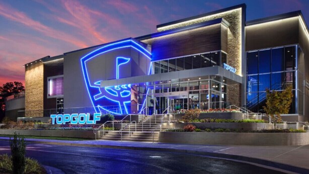A modern building with a prominent illuminated logo, a glass entrance, and a landscaped area with steps leading up to the entrance. - King Bed, 5 min walk Truist Park | The Battery (Smyrna)