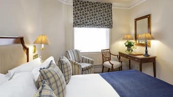 A hotel room with a large bed, a desk, two chairs, a window with a patterned curtain, and two lamps.