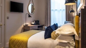 A hotel room with a bed, a desk, a TV, a mirror, and a lamp. - Sloane Place (London)