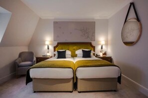 Cama doble con cabecera, lámparas de noche y una silla en una habitación con techo inclinado y un cuadro abstracto de gran tamaño.