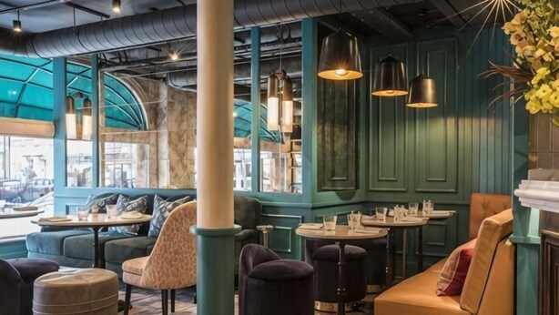 A cozy cafe with green walls, multiple seating areas including a sofa and tables, and pendant lighting. - Sloane Place (London)
