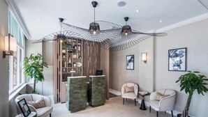A modern reception area with a desk, chairs, a plant, and a unique ceiling light fixture. - Sloane Place (London)