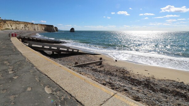 A coastal road with a guardrail, a wooden bench, and a rocky beach. - Whitfield P1 (Yarmouth)