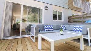 A covered patio with a white table, grey sofa with blue and white chevron cushions, and a bottle of wine. - Whitfield P1 (Yarmouth)