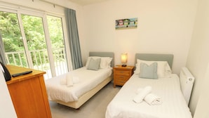A hotel room with two single beds, a wooden desk, a nightstand with a lamp, and a painting on the wall. - Whitfield P1 (Yarmouth)