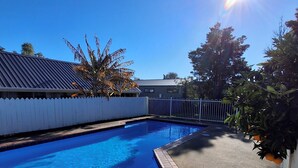 A swimming pool with a clear blue water, surrounded by a brick border and a white picket fence. - cherry grove motel (Havelock North)