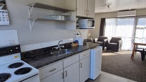 A modern kitchen with white cabinets, a built-in microwave, and a stove. There is a dining area with a table and chairs, and a large window providing natural light. - cherry grove motel (Havelock North)