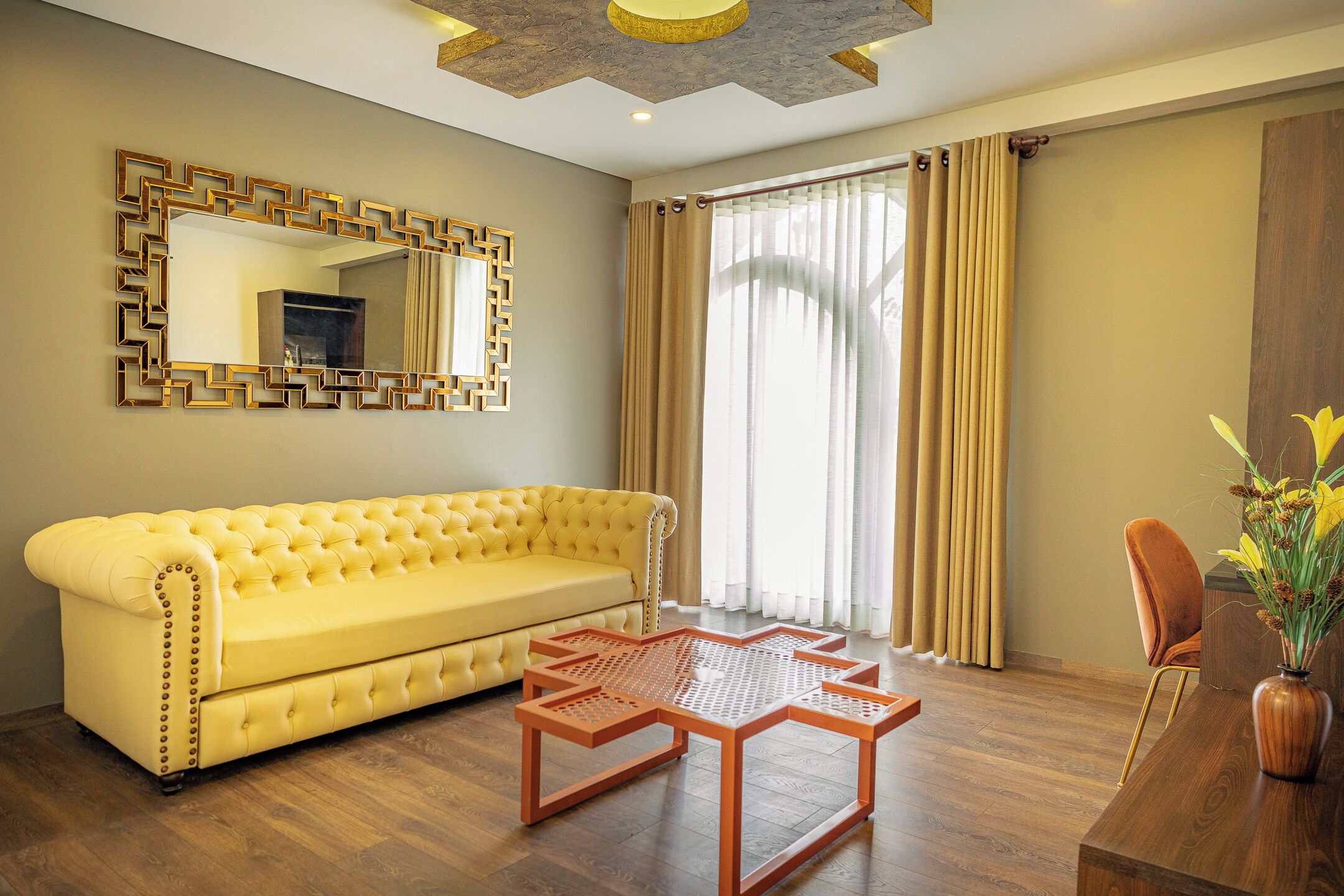 A yellow sofa, a wooden coffee table, a wooden side table, a vase with flowers, and a mirror with a geometric frame.