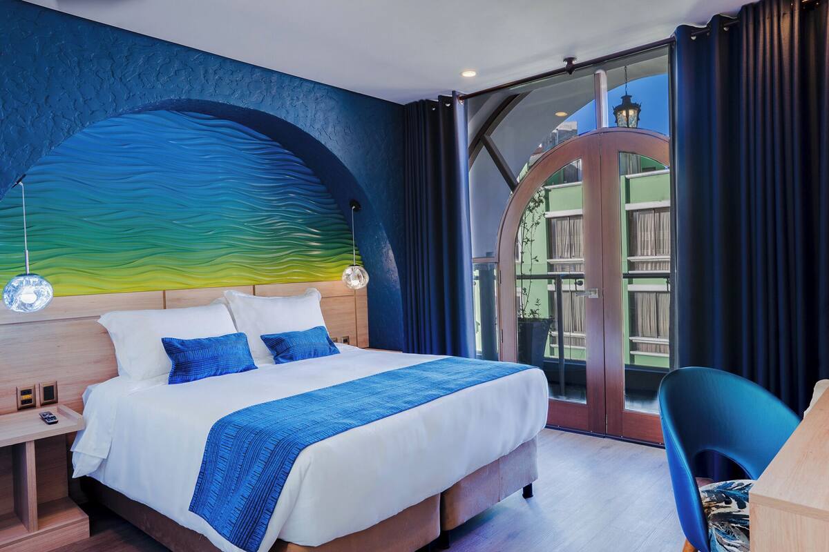 Quarto de hotel moderno com uma cama grande, uma escrivaninha e vista para o exterior.
