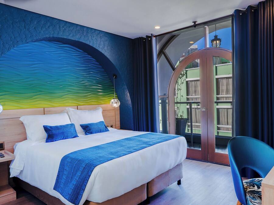 A modern hotel room with a large bed, a desk, and a view of the outdoors.