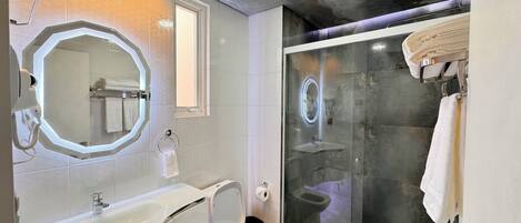 A modern bathroom with a glass-enclosed shower, a large oval mirror, and a white sink.