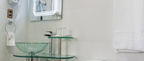 Un baño moderno con un lavabo de vidrio, un inodoro blanco y un espejo con iluminación perimetral.