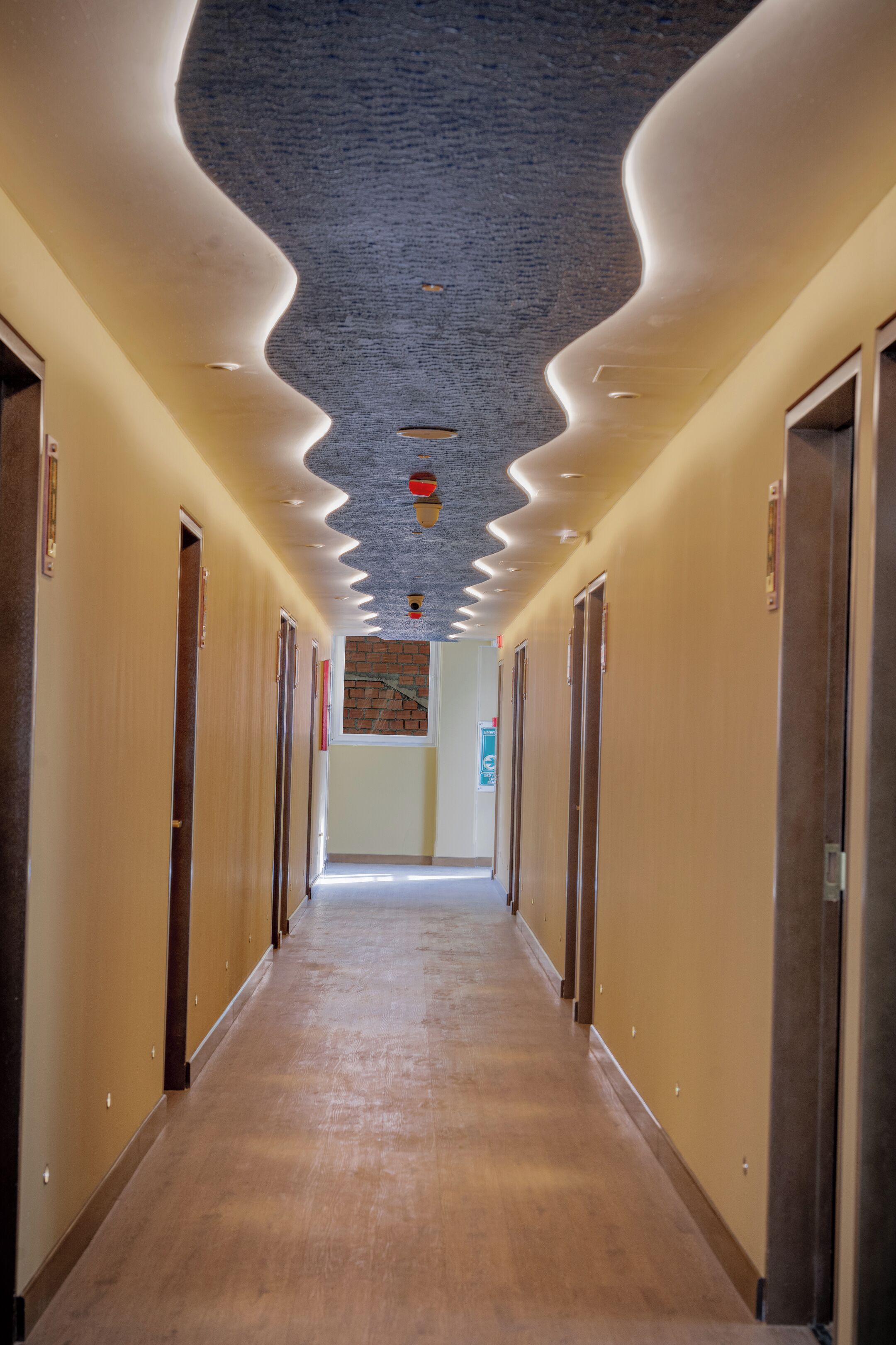 A long, narrow hallway with wooden floors and walls, leading to a door at the end.