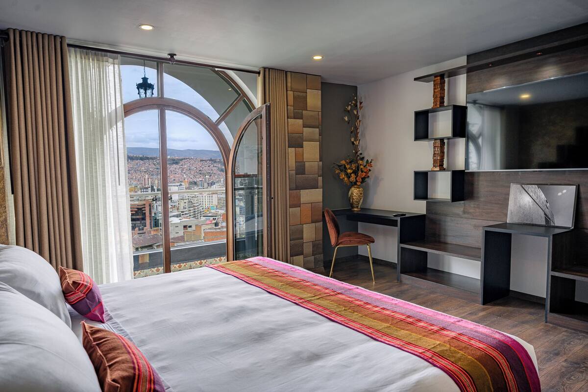 Quarto de hotel moderno com uma cama grande, uma escrivaninha e vista para a cidade.