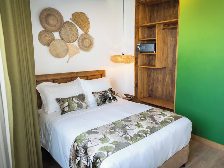 A neatly made bed with white linens and a leaf-patterned bedspread, a wooden nightstand with a lamp, and a wall with woven baskets.