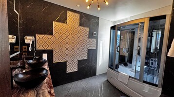 Un baño moderno con un espejo grande, un lavamanos negro y una ducha con paredes de vidrio.