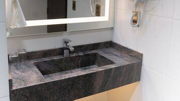 Un baño con lavamanos de mármol, un espejo grande con luz y un secador de pelo montado en la pared.