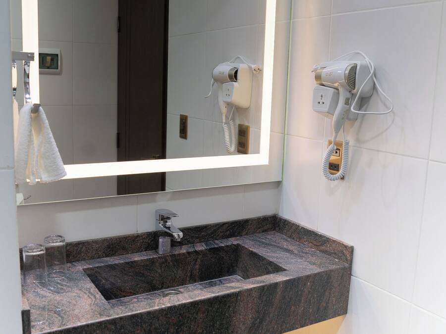 Un baño con lavamanos de mármol, un espejo grande con luz y un secador de pelo montado en la pared.