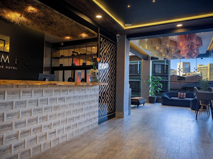 A modern hotel lobby with a brick reception desk, a decorative wall, and a seating area with a view of the cityscape.