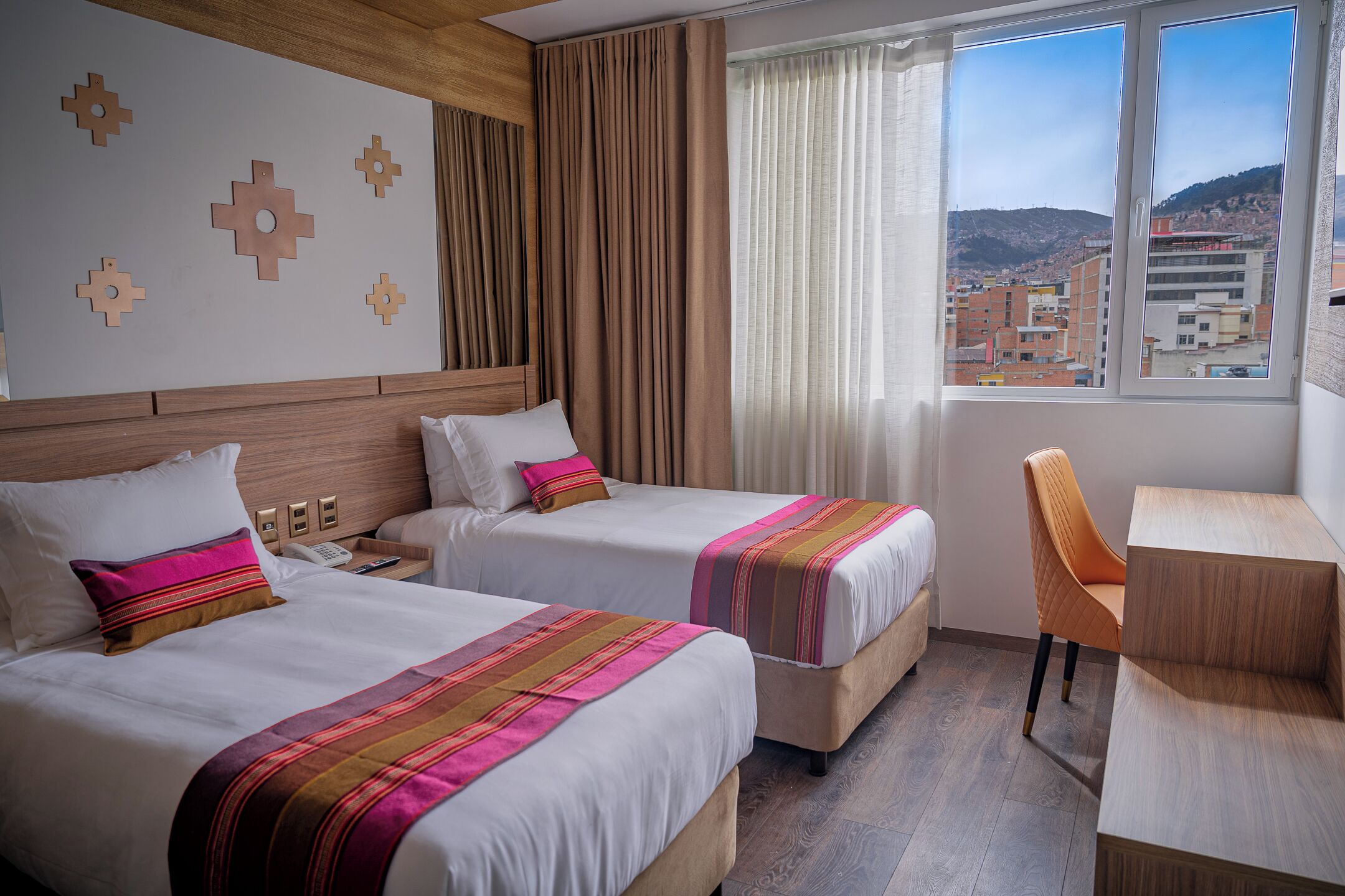 A hotel room with two beds, a desk, and a view of a cityscape.